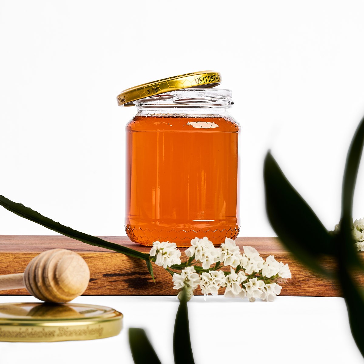 Produktfotografie eines Honigglases mit Honiglöffel und Blüten, hochwertig inszeniert für Marken und Onlineshops.