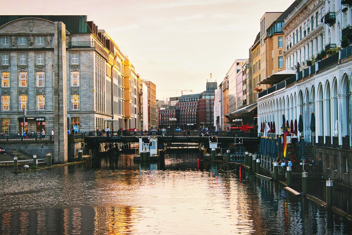 Stadtansicht der Hamburger Alsterarkaden bei Sonnenuntergang mit historischer Architektur und urbanem Wasserlauf.