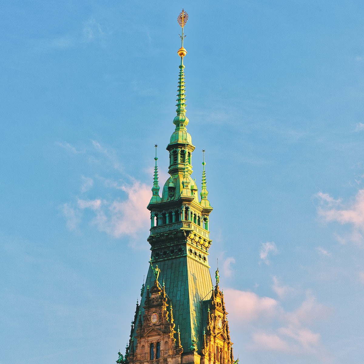 Detailaufnahme der Turmspitze des Hamburger Rathauses im Abendlicht mit historischer Architektur und blauem Himmel.