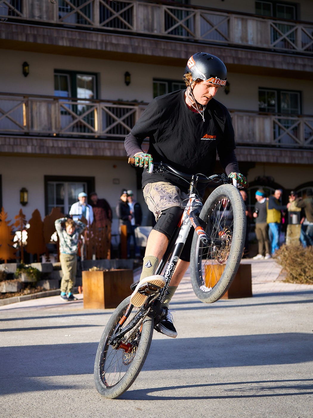Mountainbiker bei einer Bike-Show vor alpinem Hotel – actionreiche Tourismusfotografie für Outdoor- und Bikeurlaub.
