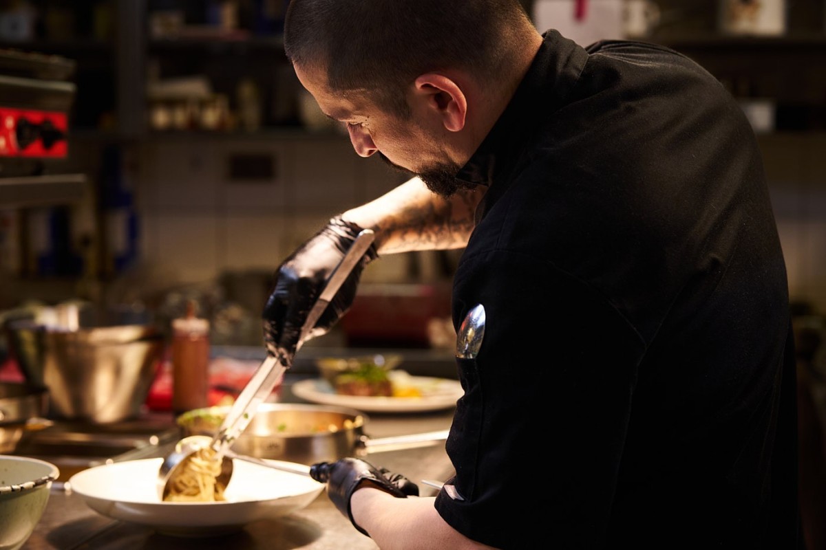 Mitarbeiterfoto eines Kochs beim Anrichten eines Pastagerichts in einer Restaurantküche – authentische Arbeitssituation in der Gastronomie.