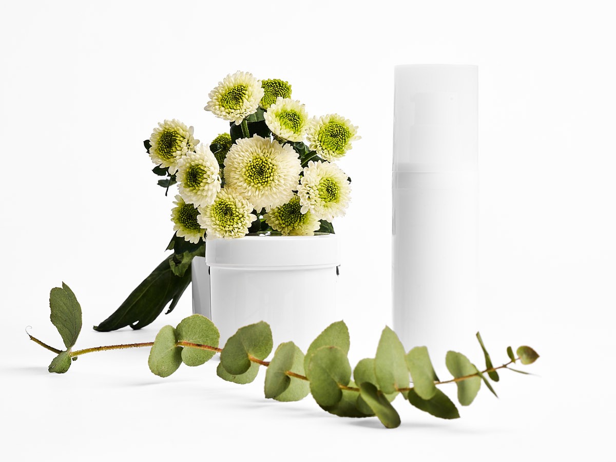 Minimalistische Produktfotografie eines Kosmetik Mockups mit weißem Tiegel und Flakon, kombiniert mit Blumen und Eukalyptus