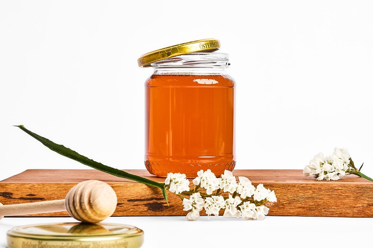 hochwertige Produktfotografie eines Honigglases mit Holzlöffel, kombiniert mit Blüten und natürlichem licht, food styling