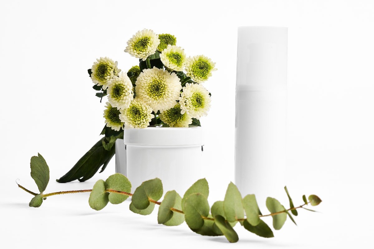 Minimalistische Produktfotografie eines Kosmetik Mockups mit weißem Tiegel und Flakon, kombiniert mit Blumen und Eukalyptus, Studio Setting