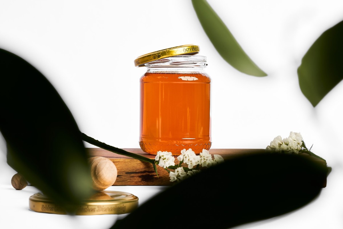 Produktfotografie von Honigglas mit Blüten und Holzlöffel, natürliches Styling im Studio für Food Branding