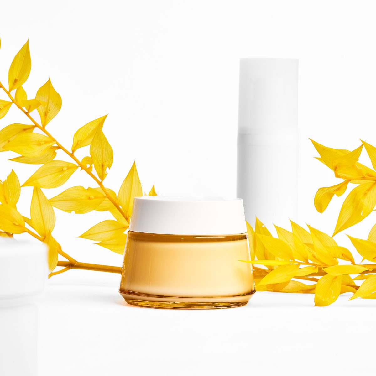 Minimalistische Produktfotografie von Kosmetik Creme und Flakon mit gelben Blättern, cleanes Studio Setup für Beauty Branding